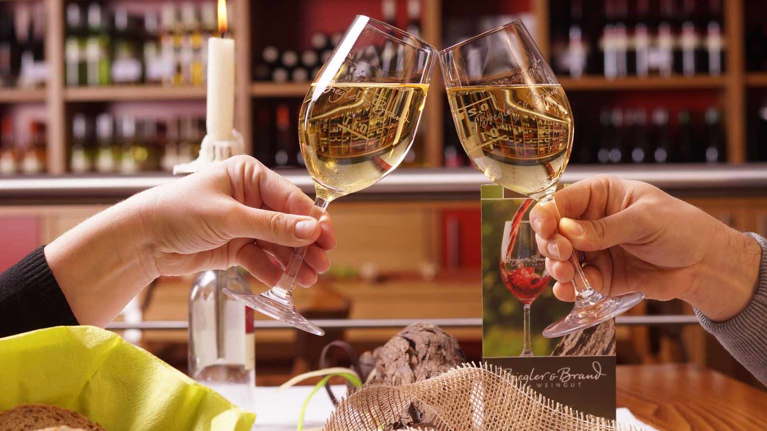 Weinprobe im Weinrestaurant & Vinothek Kaisergarten am eingedeckten Tische prosten sich zwei Personen mit zwei gefuellten Weissweinglaesern zu